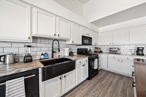 A modern kitchen with white cabinets, a black stove, a microwave, a sink, and a coffee maker.