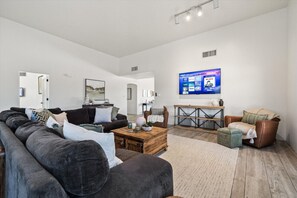 A modern living room with a sectional sofa, a wooden coffee table, and a television mounted on the wall. - 4BR Home w/ Mountain Views, Pool, Spa, Firepit & Gazebo (Tucson)