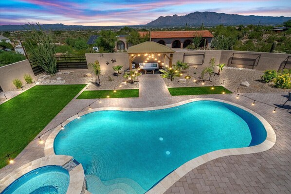 A swimming pool with a patio area, a covered seating area, and a view of mountains in the background. - 4BR Home w/ Mountain Views, Pool, Spa, Firepit & Gazebo (Tucson)
