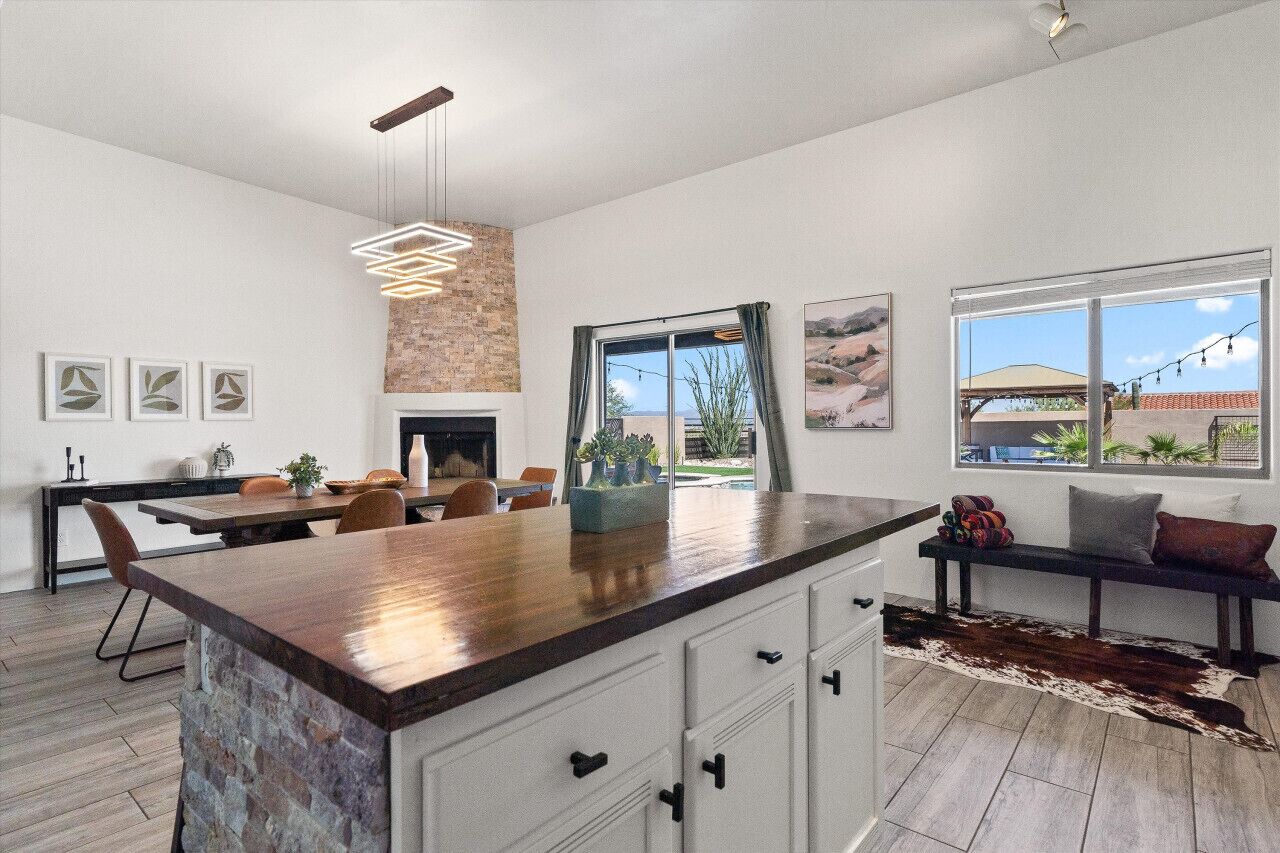 A modern kitchen with a central island, a dining area with chairs, a fireplace, and a view of the outdoors.