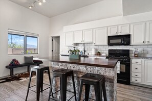 A modern kitchen with white cabinets, a granite countertop, and a large island with bar stools. - 4BR Home w/ Mountain Views, Pool, Spa, Firepit & Gazebo (Tucson)