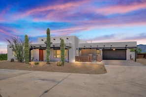 A modern two-story house with a garage, surrounded by desert vegetation. - 4BR Home w/ Mountain Views, Pool, Spa, Firepit & Gazebo (Tucson)