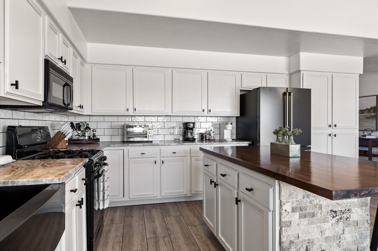 A modern kitchen with white cabinetry, a granite countertop, a stainless steel refrigerator, and a built-in oven.