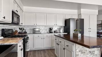 A modern kitchen with white cabinetry, a granite countertop, a stainless steel refrigerator, and a built-in oven.