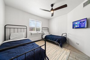 A room with two beds, a ceiling fan, a window with blinds, and a mounted TV displaying streaming services.