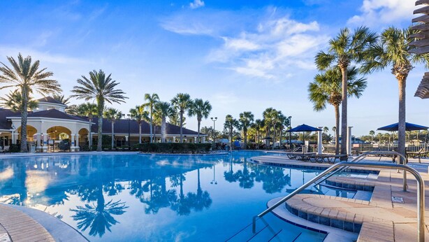 A large, clear swimming pool with palm trees and a covered area with umbrellas. - Gorgeous Vacation Home With Pool Close To Disney (Kissimmee)
