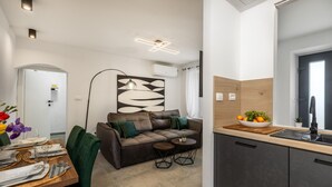 A modern living room with a brown leather sofa, a dining table set with plates and cutlery, and a small round table with a glass. A kitchen area is visible with a bowl of fruit on the counter. - 1 bedroom cozy home in Hreljin (Hreljin)