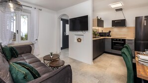 A modern kitchen with a flat-screen TV, a built-in oven, and a refrigerator. There is a dining area with a table and chairs, and a living room with a sofa and a coffee table. - 1 bedroom cozy home in Hreljin (Hreljin)