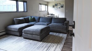 A living room with a sectional sofa, a dining table with chairs, and a rug. - The Denali Nook in UMED District & University prk! (Anchorage)