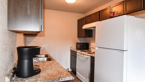 A compact kitchen with granite countertops, a black coffee maker, a microwave, a stove, and a white refrigerator. - The Denali Nook in UMED District & University prk! (Anchorage)