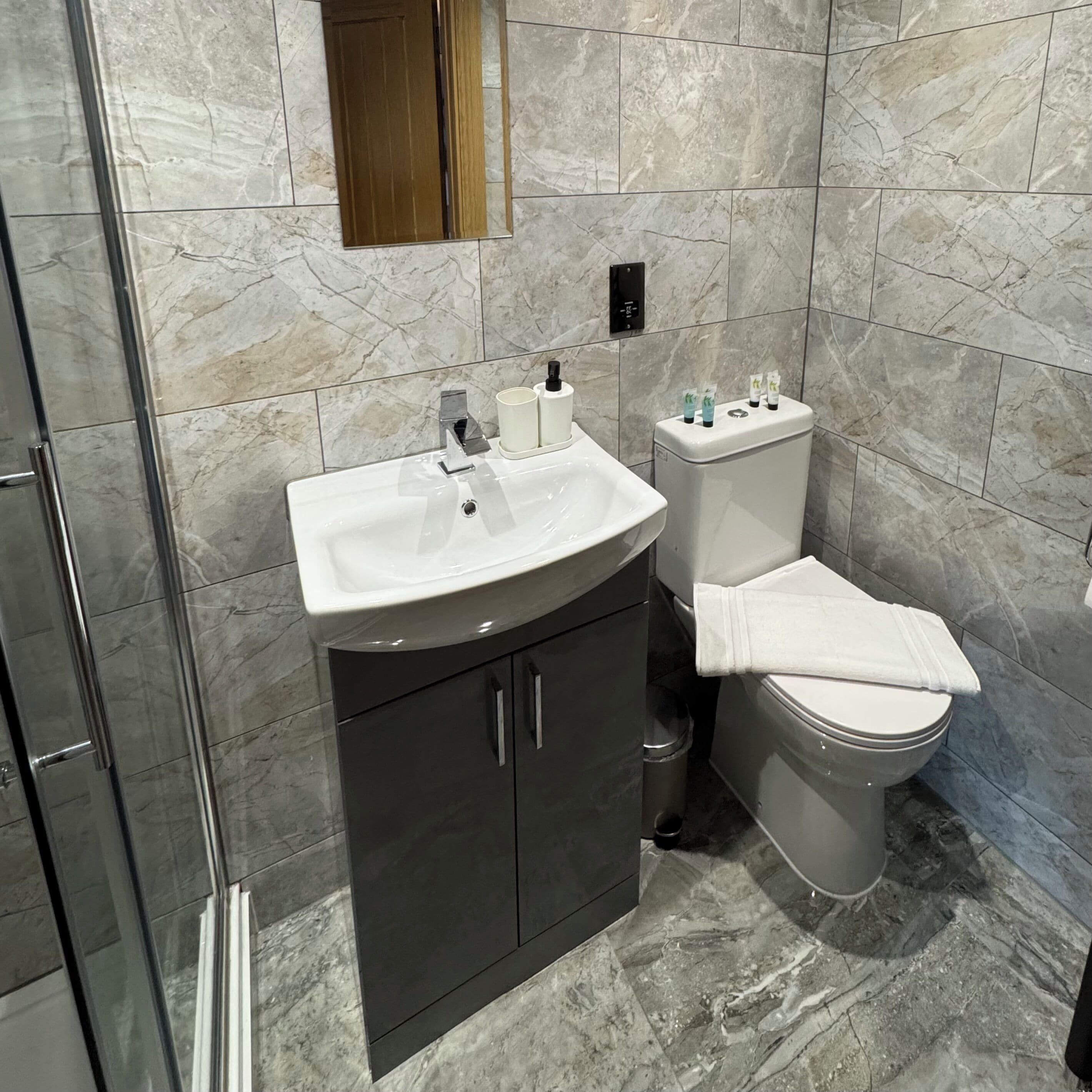 Un baño moderno con lavamanos de mármol, inodoro y cabina de ducha de vidrio.