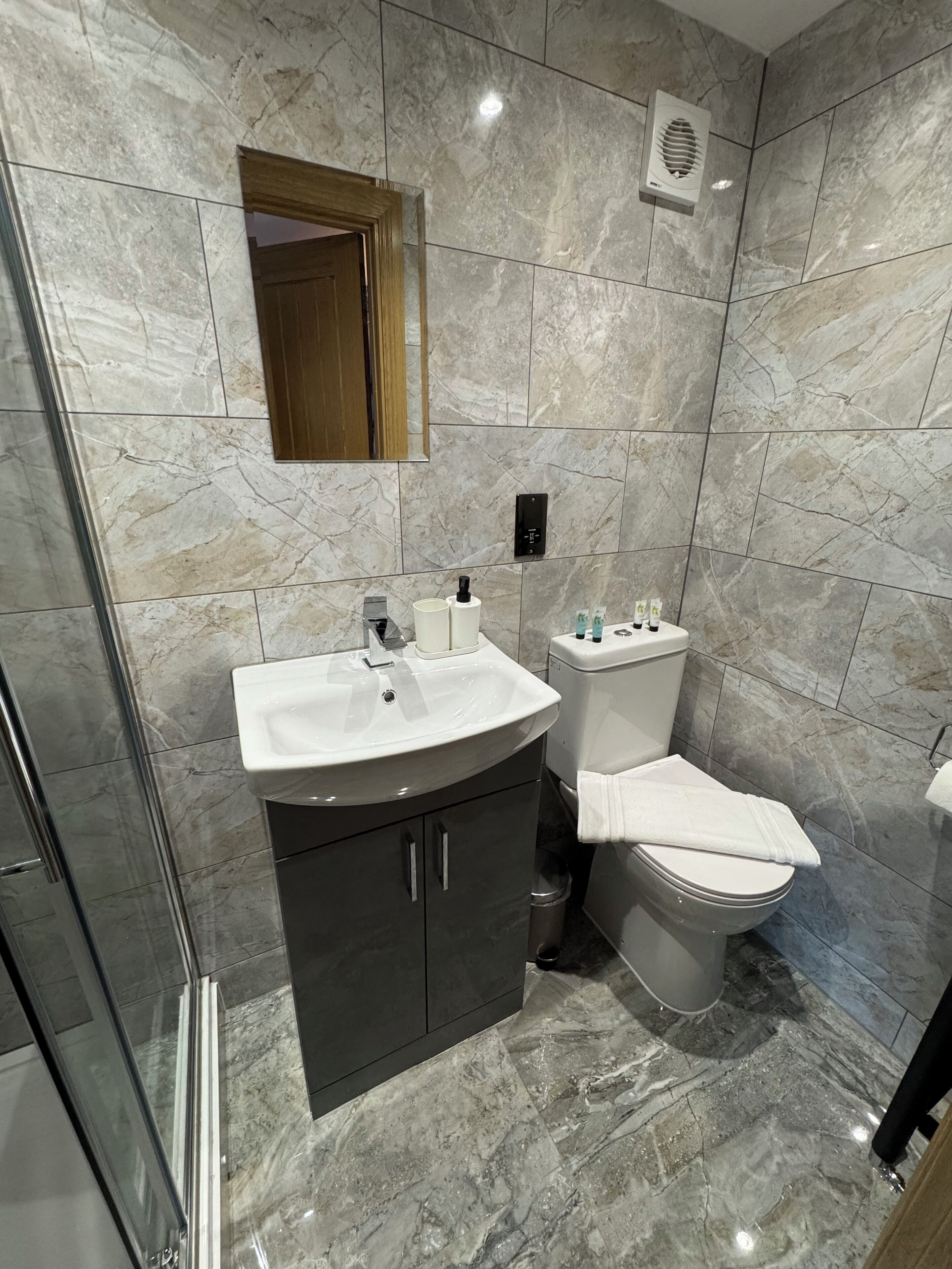 Une salle de bain moderne avec un lavabo en marbre, des meubles sombres, des toilettes et une douche à parois de verre.