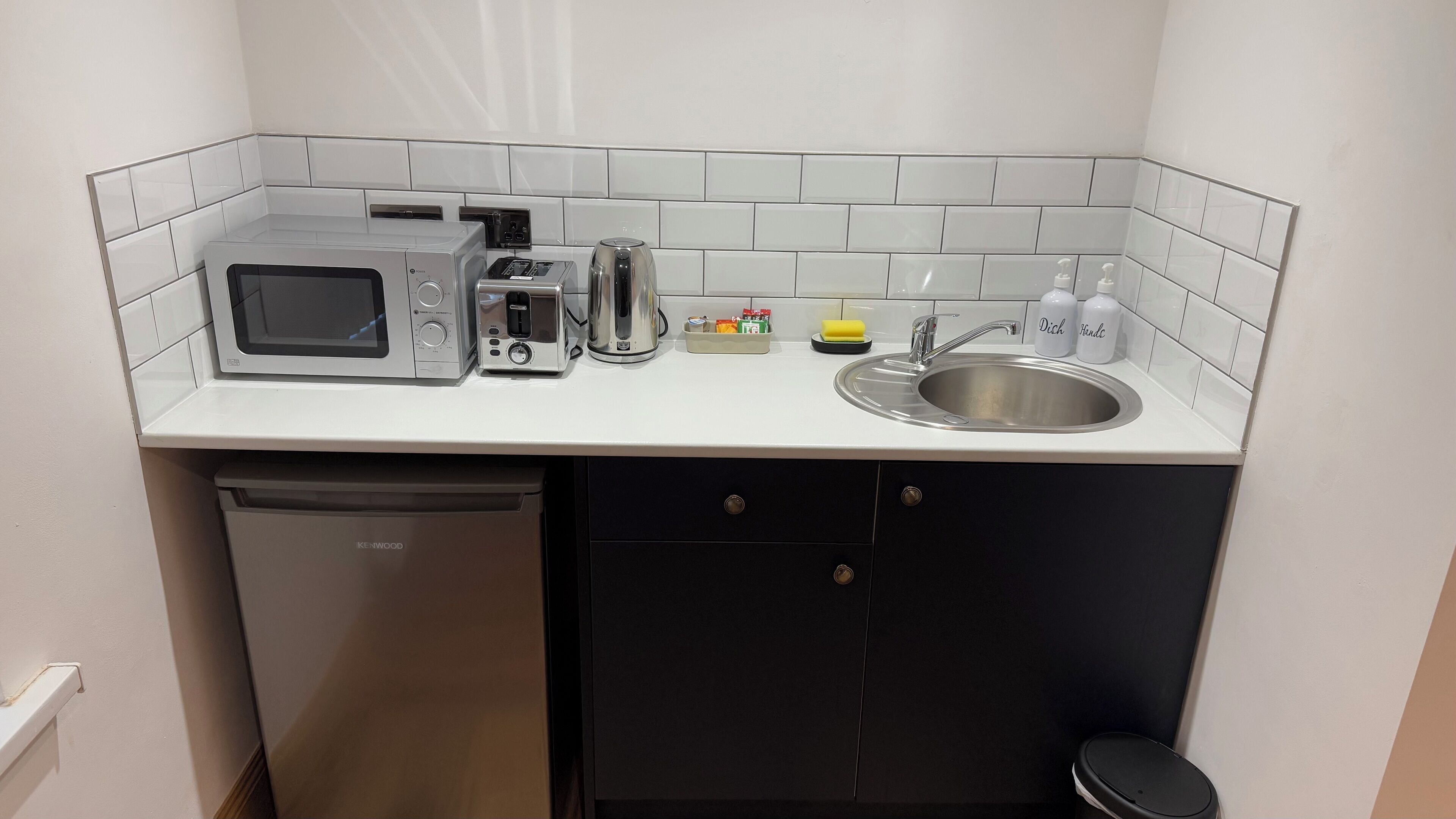 A compact kitchen with a microwave, toaster, kettle, and sink.