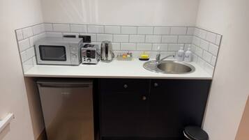 A compact kitchen with a microwave, toaster, kettle, and sink.