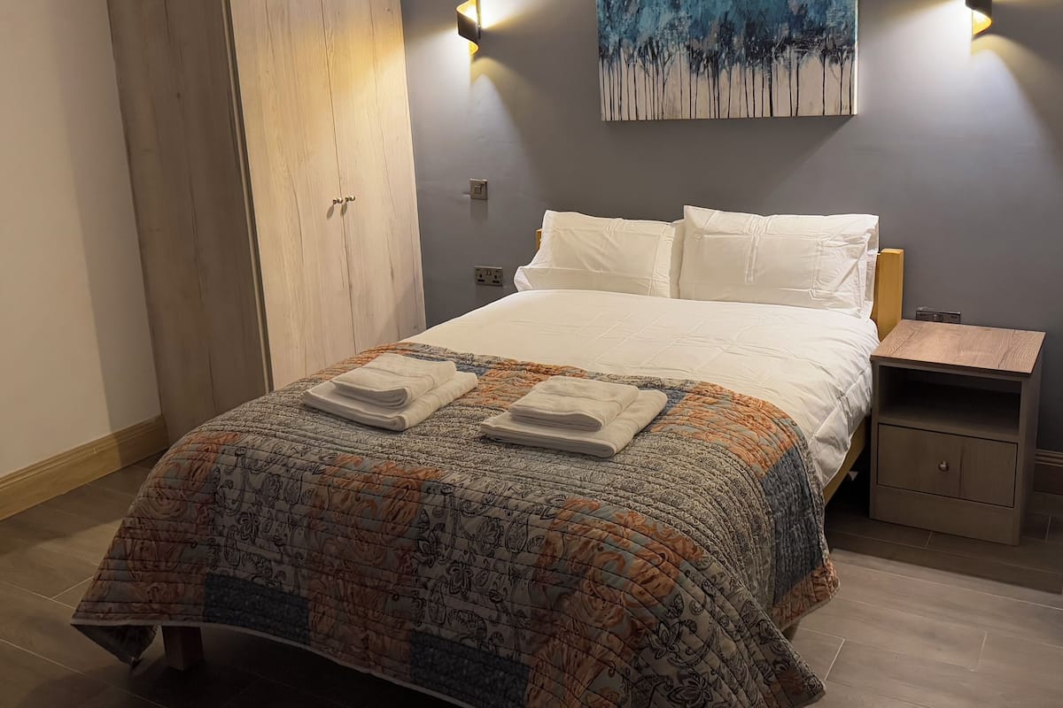 A bedroom with a bed, a wardrobe, a nightstand, and a painting on the wall.