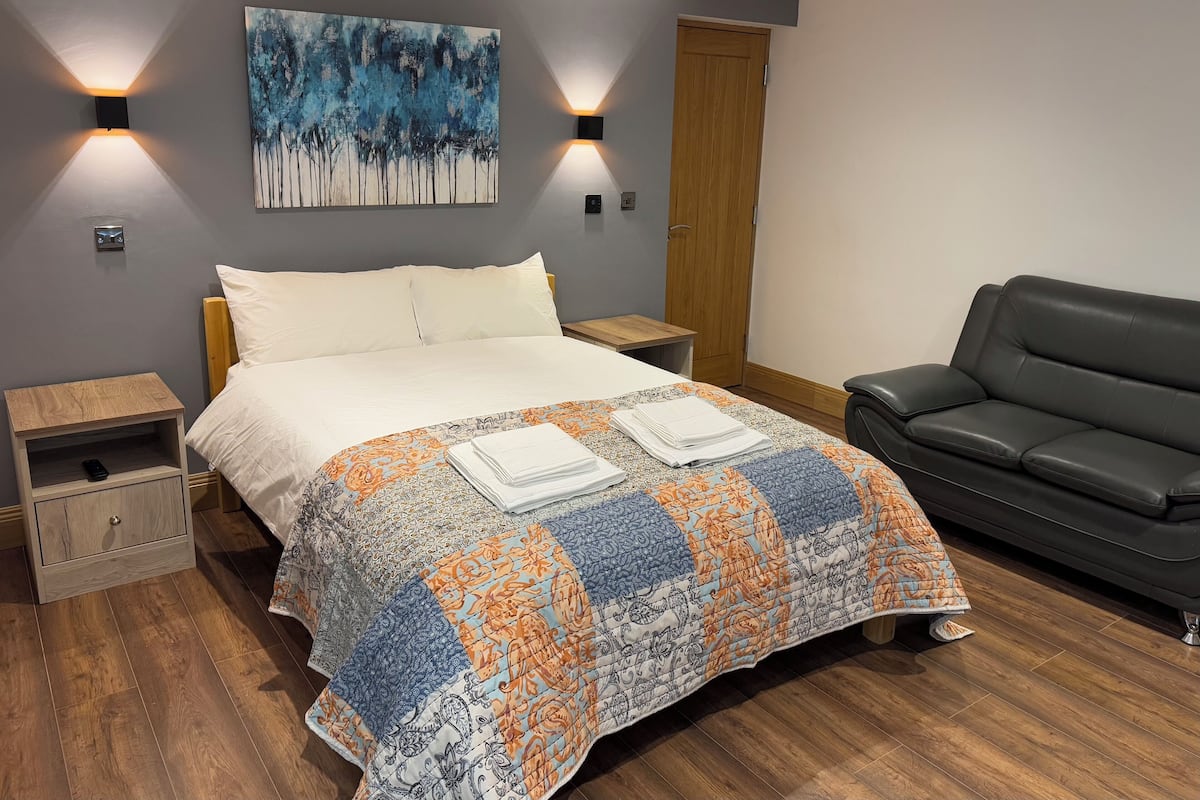 A neatly arranged bedroom with a bed, a black leather chair, and a painting on the wall.