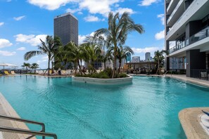A swimming pool with palm trees, a city skyline, and modern buildings in the background. - IONICA RESIDENCES at 601 NE CONDO (Miami)