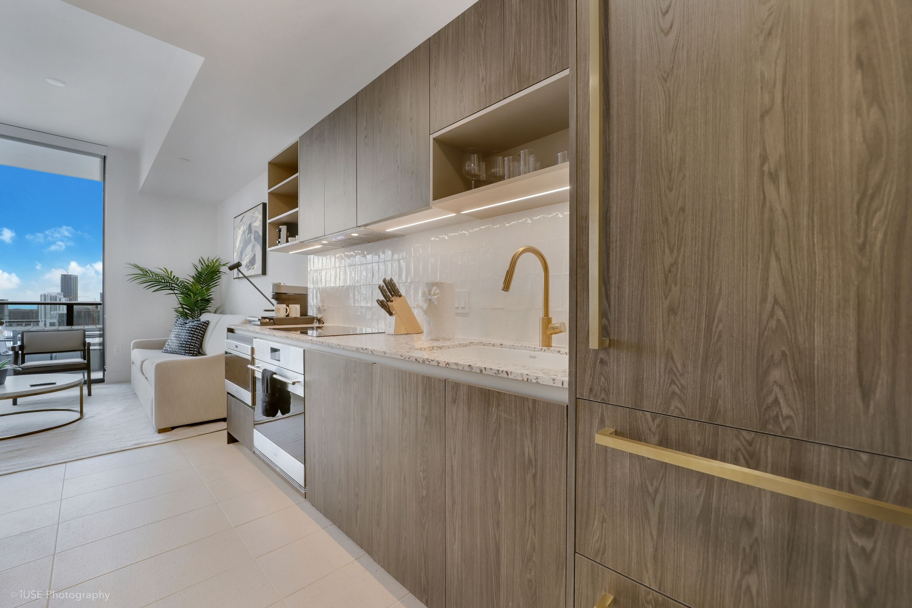 Une cuisine moderne avec des meubles en bois, un plan de travail blanc et une grande fenêtre donnant sur la ville.