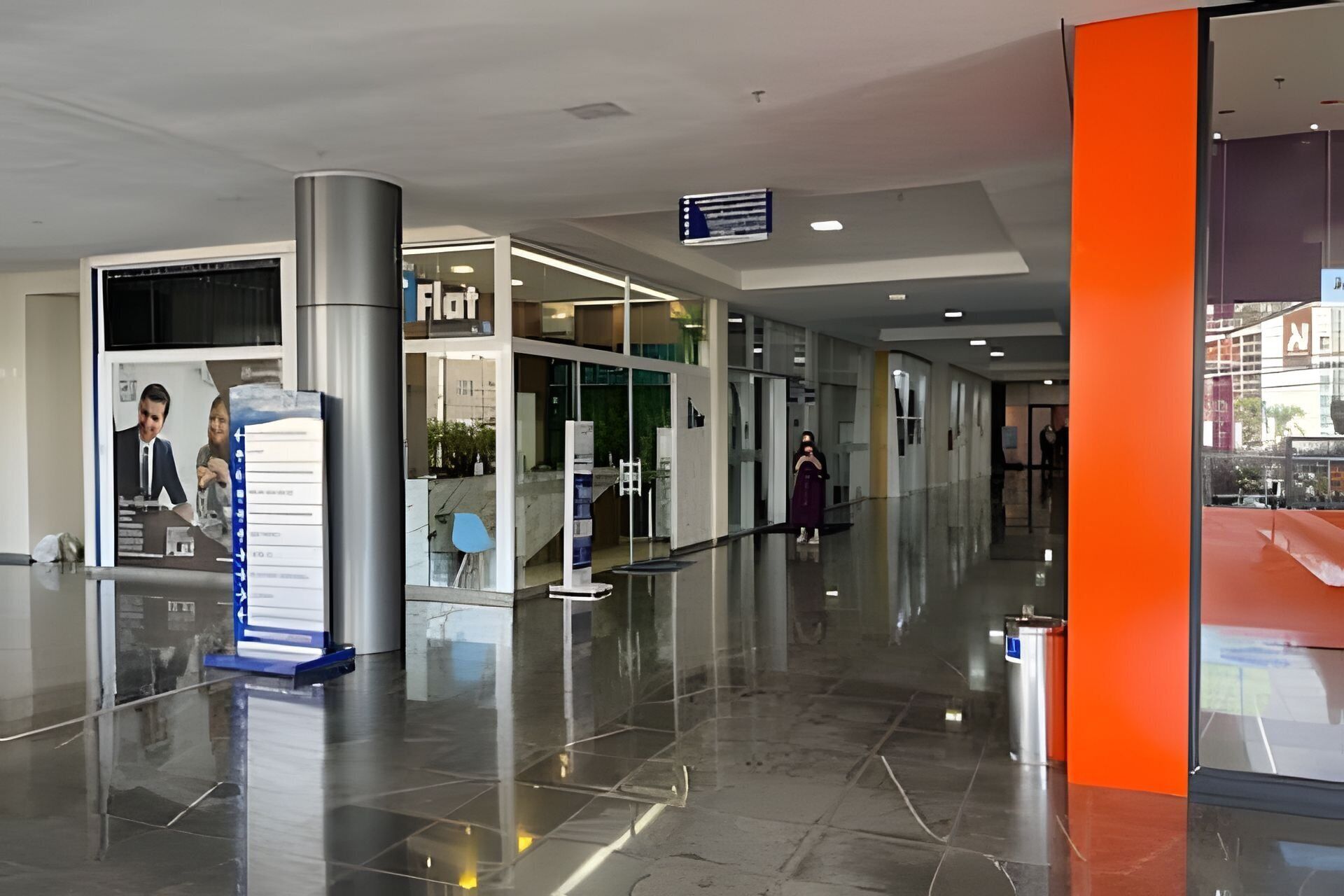 Um espaço interior moderno com piso polido, entrada visível para uma loja chamada 'Fiat' e um caminho claro que leva a uma parede laranja.