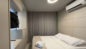 Una habitación de hotel con una cama, un televisor fijado a la pared y un equipo de aire acondicionado.