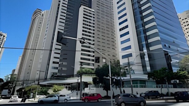 Un paisaje urbano con edificios altos y modernos, un cielo azul despejado y una calle con coches.