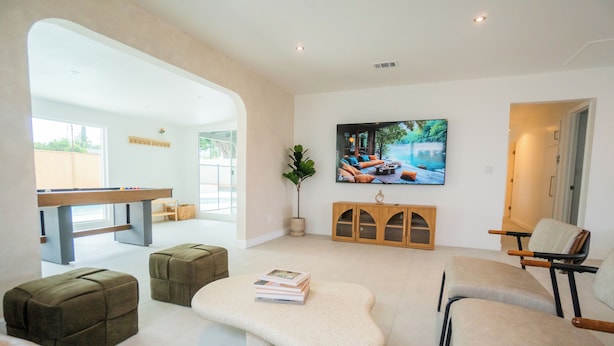 A modern living room with a pool table, comfortable seating, a flat-screen TV, and a large window.