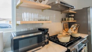 A modern kitchen with a built-in microwave, coffee maker, stove, and shelves with glassware and pots.