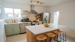A modern kitchen with a central island, bar stools, stainless steel appliances, and a view through the window.