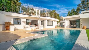 Une maison moderne dotée d’une piscine, d’un espace salon extérieur et offrant une vue sur les arbres environnants.
