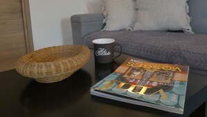 A magazine on a table, a wicker basket, a coffee mug, and a grey sofa with pillows.