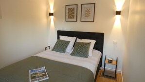 A neatly made bed with a magazine, two wall-mounted lamps, and a framed picture on the wall.