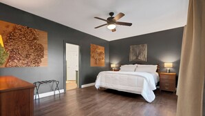Une chambre à coucher avec un lit, des tables de chevet, un ventilateur de plafond et des œuvres d’art accrochées aux murs.