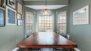 Une salle à manger avec une longue table en bois, des chaises noires et un luminaire suspendu.