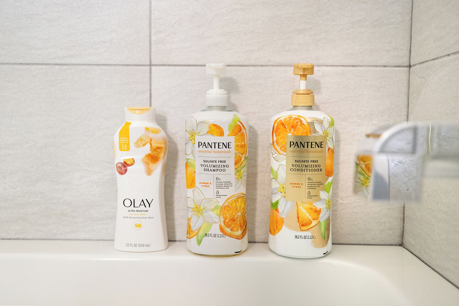 Tres botellas de productos para el cabello Olay y Pantene sobre una repisa de baño.