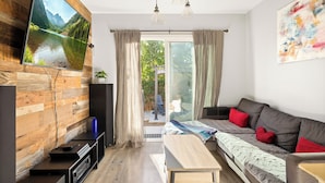 Una sala de estar moderna con una pared de madera, un televisor grande, un sofá con cojines rojos y un banco.