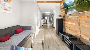 Una sala de estar moderna con un sofá gris, cojines rojos, una pared de acento de madera y un televisor grande.