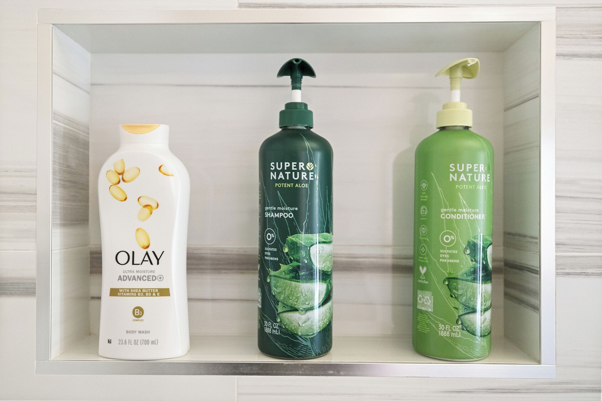 Een badkamerschaar met drie flessen haarverzorgingsproducten: Olay Advanced Body Wash, Super Nature Shampoo en Super Nature Conditioner.
