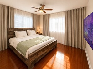 Een slaapkamer met een houten bed, een plafondventilator en een groot raam met gordijnen.