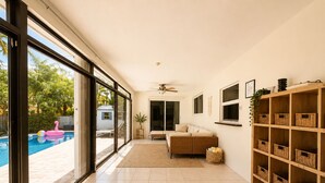 A spacious living area with a large sliding glass door leading to a pool, a ceiling fan, a sofa, and a wooden shelving unit. - ★★★★★CHARMING 3BDR VILLA W/ PRIVATE POOL & SPACIOUS BACKYARD IN HOLLYWOOD (Hollywood)