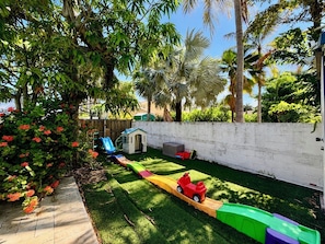 A backyard with a play area including a slide, a small house, and a toy car.