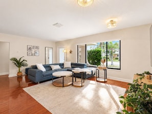 A modern living room with a blue sofa, round coffee tables, and a large window with a view of palm trees.