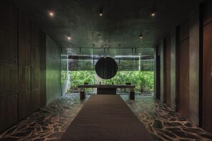 A hallway with a stone floor, wooden walls, and a central table with a hanging light fixture.