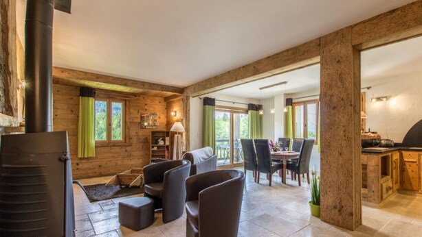 Una habitación amplia con chimenea, paredes de madera, una zona de comedor con sillas y una mesa, y un área de cocina con armarios.
