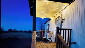 A wooden deck leading to a building with a covered porch and string lights. - Charming cottage in Springtown, TX with AC and WiFi. Enjoy your stay (Springtown)