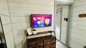 A room with a wooden wall, a wooden cabinet, a TV on the wall, and a patterned rug. - Charming cottage in Springtown, TX with AC and WiFi. Enjoy your stay (Springtown)