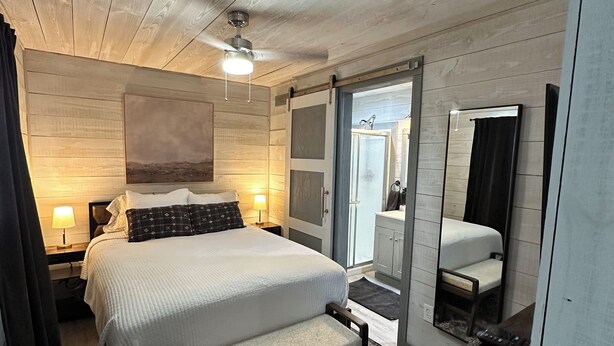A modern hotel room with a large bed, bedside tables, a desk, a mirror, and a bathroom visible through an open door. - Charming cottage in Springtown, TX with AC and WiFi. Enjoy your stay (Springtown)
