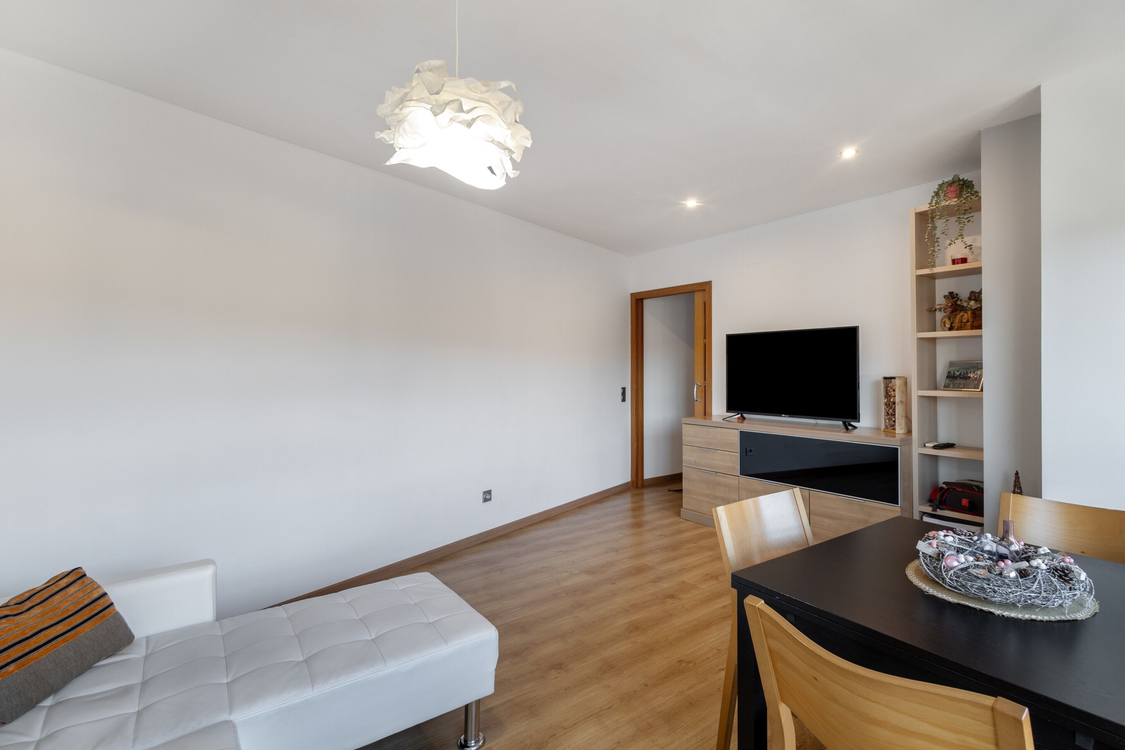 Een moderne woonkamer met een bank, een eettafel, een flatscreen televisie, houten kasten en een decoratief object op de tafel.