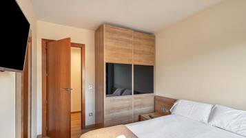 Un dormitorio con cama, armario, televisor y puerta.