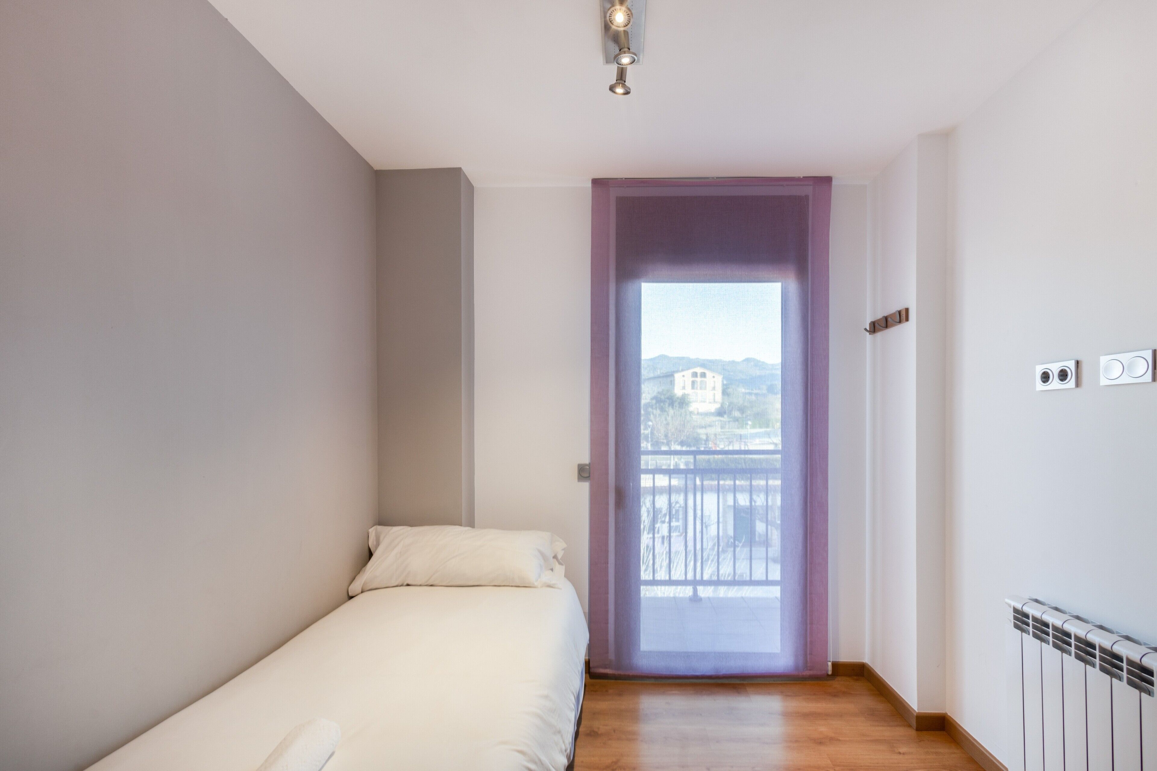Une chambre avec un lit simple, une fenêtre donnant sur un paysage agréable et un radiateur.