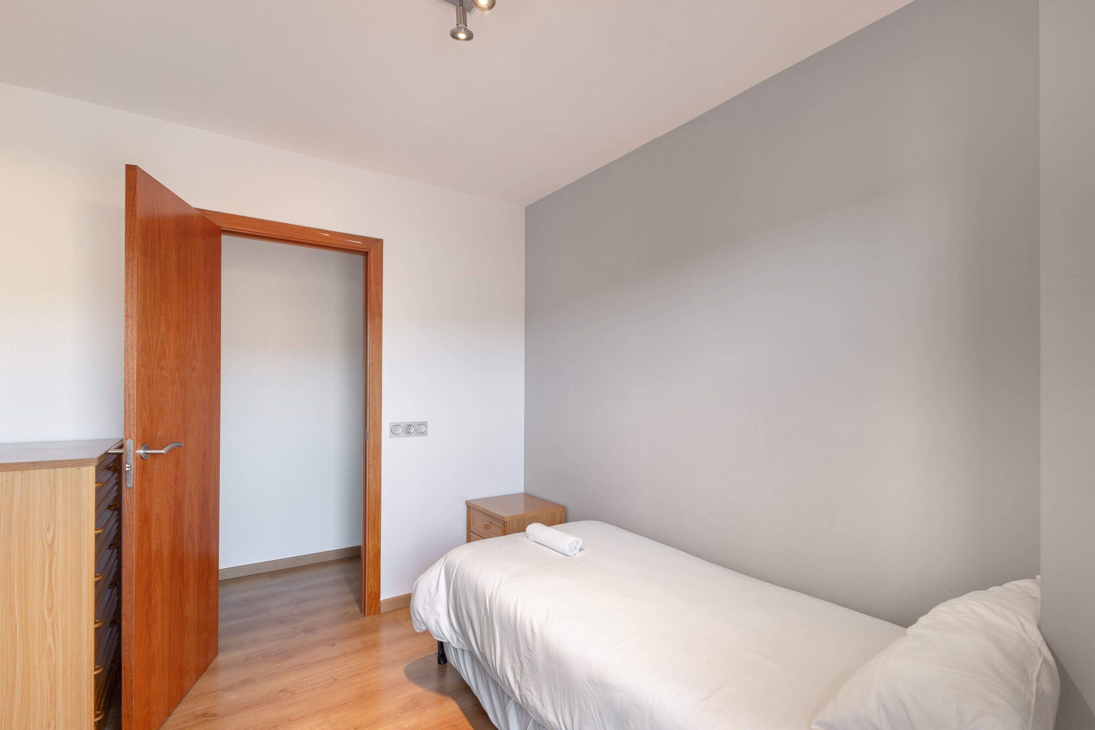 Un dormitorio con una cama, un armario de madera, una mesita de noche y una puerta que da a otra habitación.